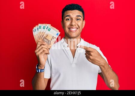 Giovane arabo che detiene 50 banconote in euro sorridendo felice di indicare con mano e dito Foto Stock