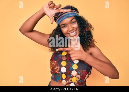 Giovane donna afroamericana in stile bohémien e hippie sorridente che fa cornice con mani e dita con viso felice. Creatività e fotografia Foto Stock