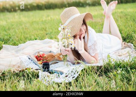 Ragazza in un campo con margherite, estate nel village.Young sorridente donna che si rilassa all'aperto e che ha un picnic, è sdraiata su una coperta sul Foto Stock