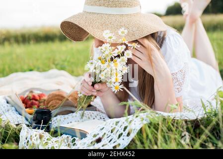 Ragazza in un campo con margherite, estate nel village.Young sorridente donna che si rilassa all'aperto e che ha un picnic, è sdraiata su una coperta sul Foto Stock