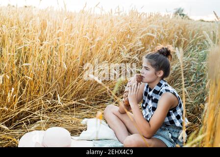 Bambino felice con pane in campo giallo di grano autunnale. Un campo con ears.girl maturo siede su un copriletto, frutta fresca e bacche, pane e panini in un Foto Stock