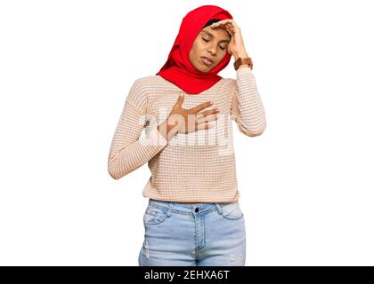 Giovane donna afroamericana che indossa la tradizionale sciarpa islamica dell'hijab che tocca la fronte per la malattia e la febbre, l'influenza e il freddo, il virus malato Foto Stock