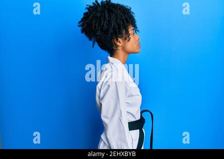 Donna afroamericana con capelli afro che indossa kimono karate e cintura nera guardando a lato, profilo relax posa con viso naturale con sorriso sicuro. Foto Stock