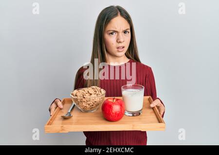 Bella bruna bambina che tiene il vassoio con il cibo di colazione indeceless e l'espressione confusa. Concetto di dubbio. Foto Stock