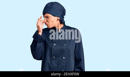 Giovane donna bruna con capelli corti indossando cuoco professionale uniforme odore qualcosa di stinoso e disgustoso, odore intollerabile, respiro strugge Foto Stock