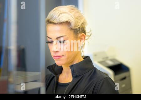 Bella fit sana bionda donna d'affari di mezza età in posa con gli occhi calati e un sorriso tranquillo in ufficio in un vicino su testa e spalle porta Foto Stock