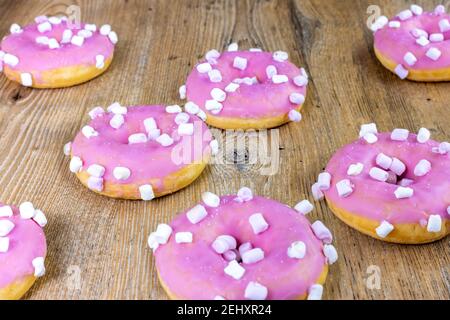 ciambelle rosa con marshmallows bianchi disposte casualmente su tavolo di legno Foto Stock