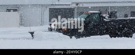 Un camion nero di proprietà di un appaltatore privato sta arando la neve nel parcheggio di un'azienda durante una tempesta di neve. Foto Stock