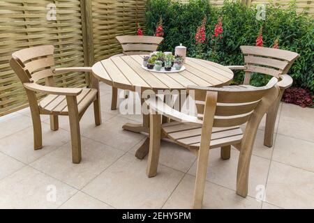 Area esterna in legno per pranzare, giardino con mobili da giardino, patio pavimentato in pietra moderno - tavolo e sedie espongono piante succulente in vasi di ceramica UK Foto Stock