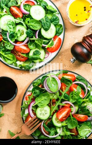 Insalata verde primaverile con spinaci, pomodori ciliegini, insalata di mais e cipolla rossa. Concetto di cibo sano. Tavolo in pietra beige. Vista dall'alto. Spazio di copia Foto Stock