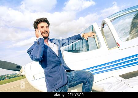 Giovane bell'uomo che parla con lo smartphone al privato Aereo: Concetto aziendale moderno con un ragazzo sicuro che utilizza lo smartphone in aeroporto Foto Stock