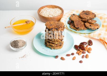 frittelle di banana di farina d'avena con semi di chia, mandorle, prugne e datteri, conditi con miele e noci tritate su uno sfondo leggero. dieta colazione sana Foto Stock