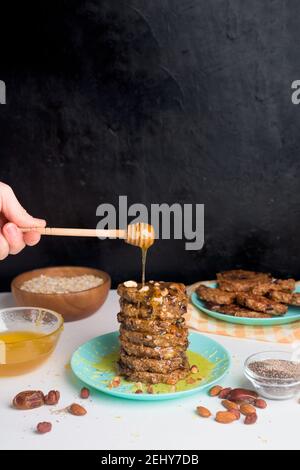 frittelle fatte in casa con semi di chia, mandorle, prugne e datteri, condite con miele e noci schiacciate su sfondo scuro. colazione dietetica Foto Stock