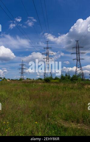 Piloni di linee di trasmissione di potenza ad alta tensione su un campo estivo con cielo blu e nuvole Foto Stock
