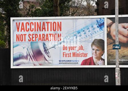 Greenock, Scozia, Regno Unito. 20 febbraio 2021. Nella foto: Immagine del primo ministro scozzese Nicola Sturgeon con la grafica di un vaccino COVID19 e una siringa con lo slogan: "VACCINAZIONE NON SEPARAZIONE. FAI IL TUO LAVORO, PRIMO MINISTRO." su un cartellone nel mezzo di Greenock, in un crocevia trafficato di Brougham St & Campbell St. Questo è in riferimento alla maggioranza silenziosa di persone in Scozia che si oppongono alla SNP cercando un secondo referendum sull'indipendenza nel mezzo di una pandemia che lo ha fatto Nel Regno Unito sono state uccise oltre 106,000 persone, di cui 6,816 nella sola Scozia. Credit: Colin Fisher/Alamy Live News. Foto Stock