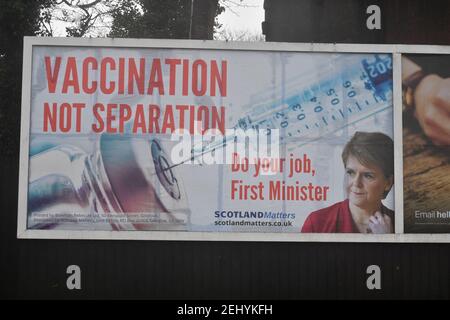 Greenock, Scozia, Regno Unito. 20 febbraio 2021. Nella foto: Immagine del primo ministro scozzese Nicola Sturgeon con la grafica di un vaccino COVID19 e una siringa con lo slogan: "VACCINAZIONE NON SEPARAZIONE. FAI IL TUO LAVORO, PRIMO MINISTRO." su un cartellone nel mezzo di Greenock, in un crocevia trafficato di Brougham St & Campbell St. Questo è in riferimento alla maggioranza silenziosa di persone in Scozia che si oppongono alla SNP cercando un secondo referendum sull'indipendenza nel mezzo di una pandemia che lo ha fatto Nel Regno Unito sono state uccise oltre 106,000 persone, di cui 6,816 nella sola Scozia. Credit: Colin Fisher/Alamy Live News. Foto Stock