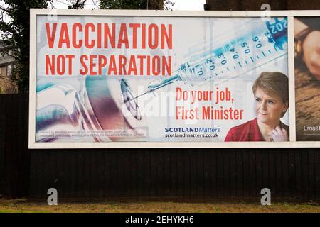 Greenock, Scozia, Regno Unito. 20 febbraio 2021. Nella foto: Immagine del primo ministro scozzese Nicola Sturgeon con la grafica di un vaccino COVID19 e una siringa con lo slogan: "VACCINAZIONE NON SEPARAZIONE. FAI IL TUO LAVORO, PRIMO MINISTRO." su un cartellone nel mezzo di Greenock, in un crocevia trafficato di Brougham St & Campbell St. Questo è in riferimento alla maggioranza silenziosa di persone in Scozia che si oppongono alla SNP cercando un secondo referendum sull'indipendenza nel mezzo di una pandemia che lo ha fatto Nel Regno Unito sono state uccise oltre 106,000 persone, di cui 6,816 nella sola Scozia. Credit: Colin Fisher/Alamy Live News. Foto Stock