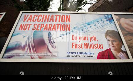 Greenock, Scozia, Regno Unito. 20 febbraio 2021. Nella foto: Immagine del primo ministro scozzese Nicola Sturgeon con la grafica di un vaccino COVID19 e una siringa con lo slogan: "VACCINAZIONE NON SEPARAZIONE. FAI IL TUO LAVORO, PRIMO MINISTRO." su un cartellone nel mezzo di Greenock, in un crocevia trafficato di Brougham St & Campbell St. Questo è in riferimento alla maggioranza silenziosa di persone in Scozia che si oppongono alla SNP cercando un secondo referendum sull'indipendenza nel mezzo di una pandemia che lo ha fatto Nel Regno Unito sono state uccise oltre 106,000 persone, di cui 6,816 nella sola Scozia. Credit: Colin Fisher/Alamy Live News. Foto Stock
