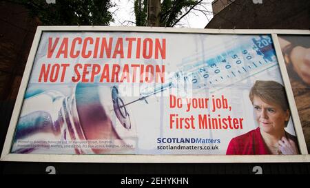 Greenock, Scozia, Regno Unito. 20 febbraio 2021. Nella foto: Immagine del primo ministro scozzese Nicola Sturgeon con la grafica di un vaccino COVID19 e una siringa con lo slogan: "VACCINAZIONE NON SEPARAZIONE. FAI IL TUO LAVORO, PRIMO MINISTRO." su un cartellone nel mezzo di Greenock, in un crocevia trafficato di Brougham St & Campbell St. Questo è in riferimento alla maggioranza silenziosa di persone in Scozia che si oppongono alla SNP cercando un secondo referendum sull'indipendenza nel mezzo di una pandemia che lo ha fatto Nel Regno Unito sono state uccise oltre 106,000 persone, di cui 6,816 nella sola Scozia. Credit: Colin Fisher/Alamy Live News. Foto Stock