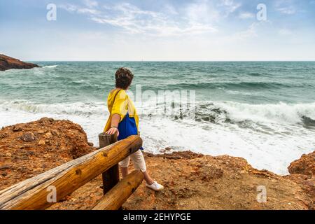 Donna appoggiata contro la ringhiera guarda le onde, a Sète in Occitania, Francia Foto Stock