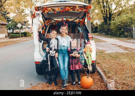 Trucco o tronco. Famiglia che celebra Halloween in tronco di auto. Madre con bambini bambini bambini che festeggiano la tradizionale vacanza all'aperto di ottobre. Sociale Foto Stock