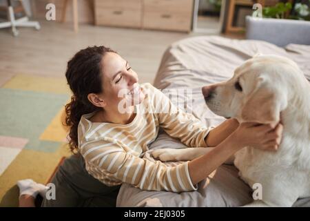 Ritratto ad alto angolo di giovane donna sorridente coccolata con cane in casa accogliente interno, spazio copia Foto Stock