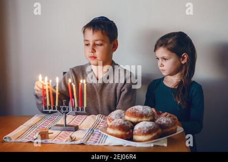 Fratelli e sorelle che illuminano le candele sulla menorah per la vacanza ebraica Hanukkah a casa. I bambini celebrano il festival delle luci di Chanukah. Sognare Foto Stock