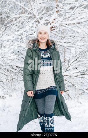 Donna in giacca verde blu parka abiti invernali, abito etnico lana modello e cappello che cammina nel parco foresta all'aperto nella giornata invernale neve. Felice da solo Foto Stock