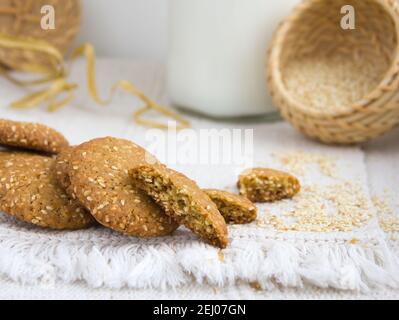 Biscotti al sesamo su un piatto bianco, semi di sesamo in un cesto di vimini, tovaglia tessuta ruvida, posa piatta, spazio copia Foto Stock