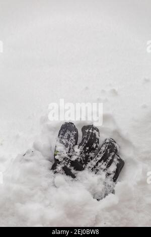 Guanto in pelle nera sulla neve con un footstep in background Foto Stock