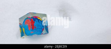 EDE, Paesi Bassi - 7 febbraio 2021: Globo in scatola cubica sdraiato nella neve. Concetto di cambiamento climatico. Foto Stock