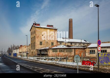 Praga, Repubblica Ceca - Febbraio 16 2021: Ex distilleria chiamata Lihovar, un edificio in rovina fatto di mattoni, un camino e una strada con segnaletica stradale Foto Stock