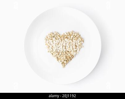 oat flakes in una forma di colpo di cuore dall'alto su un piatto bianco su sfondo bianco cibo vegetariano biologico. Foto Stock