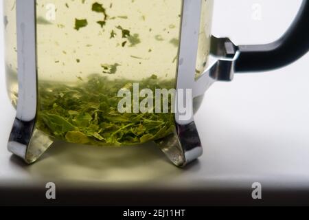 Foglie di tè verde che vengono prodotte in una teiera trasparente Foto Stock