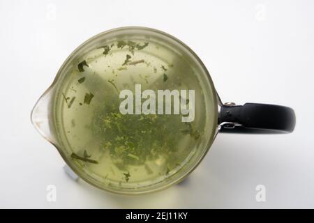 Foglie di tè verde che vengono prodotte in una teiera trasparente Foto Stock