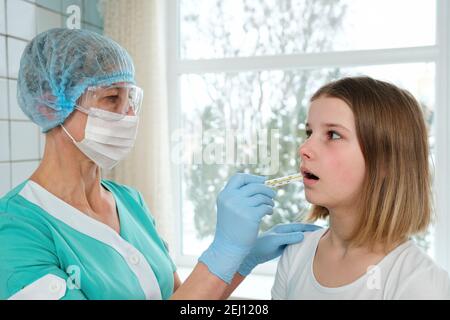 Il medico tiene il termometro nella bocca della ragazza giovane per la misurazione della temperatura. Foto Stock