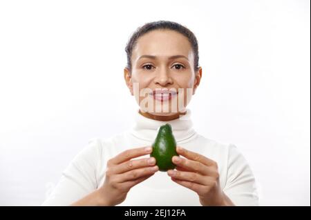 La donna bruna tiene l'avocado verde nelle mani. Frutta esotica biologica fresca naturale. Alimentazione sana, dieta di cibo crudo. Stile di vita vegetariano. nurri corretto Foto Stock
