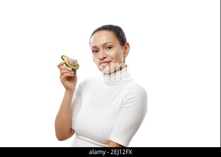 Bella donna afroamericana che posa con avocado in mano in piedi isolato su sfondo bianco. Alimentazione sana, dieta di cibo crudo. Una vita vegetariana Foto Stock