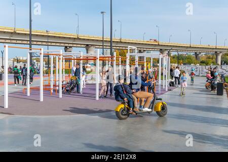 Kazan, Russia - 26 settembre 2020: Un uomo con due bambini guida uno scooter elettrico attraverso il parco della città lungo l'area di allenamento Foto Stock