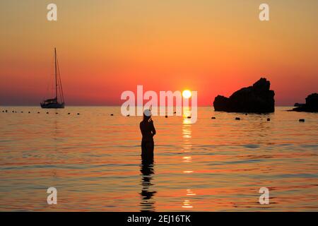 Bella ragazza di fumare una sigaretta e godendovi il tramonto sul Ghajn Tuffieha Bay di Malta Foto Stock