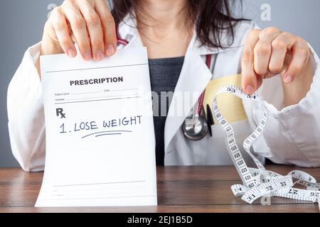 Una donna medico sta tenendo una prescrizione che dice perdere peso in una mano e un metro a nastro per addominale misurazione della circonferenza sull'altro Foto Stock