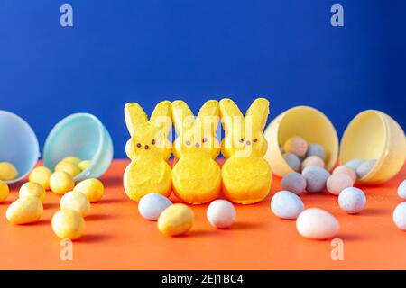 Festa di Pasqua celebrazione concetto con tre coniglietti marshmallow e. più piccole uova di pasqua colorate e croccanti ricoperte di zucchero orang Foto Stock