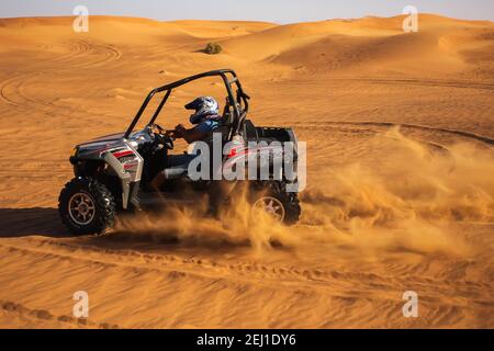 Pilota maschile in casco equitazione quad buggy a dune di sabbia del deserto, safari estremo divertimento Foto Stock