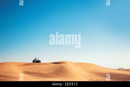 Vista minimalista del deserto con cielo blu, collina di sabbia e una moto quad buggy, avventure di sport motoristici, guida fuoristrada Foto Stock