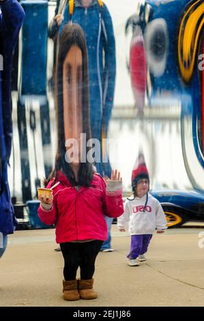 Specchio funhouse, l'immagine di una giovane ragazza che indossa una giacca rossa si riflette sulla superficie di uno specchio distorsivo a Navy Pier, Chicago, Illinois. Foto Stock