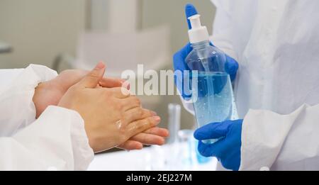 Ricercatori epidemiologici in abbigliamento protettivo anti-virus lavando le mani con gel di alcool prima di iniziare l'esperimento in un laboratorio scientifico. HY Foto Stock