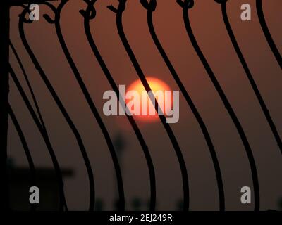 messa a fuoco selettiva di barre rustiche in metallo contro il cielo e il sole sfocati durante il tramonto, silhouette vista, sole dietro le sbarre Foto Stock