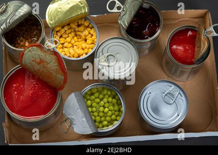 Verdure in scatola come fagioli, piselli, mais, tomatos in scatola di cartone. Lattine di stagno. Sfondo scuro. Vista dall'alto Foto Stock