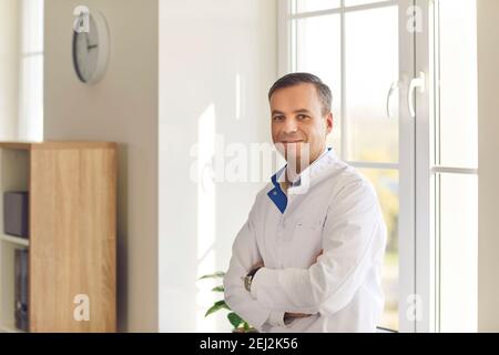 Sorridente scienziato o medico in bianco cappotto in piedi braccia incrociate in laboratorio o in ospedale Foto Stock