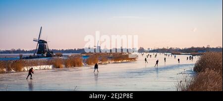 Classica scena olandese con pattinatori di ghiaccio su un lago durante un periodo freddo in inverno. Foto Stock